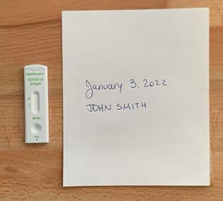 Example of a photo featuring a rapid test cassette with a positive result beside a paper on which a name and the date are handwritten.